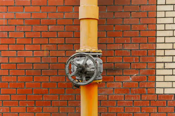 A yellow pipe with a metal valve is attached to a red brick wall.