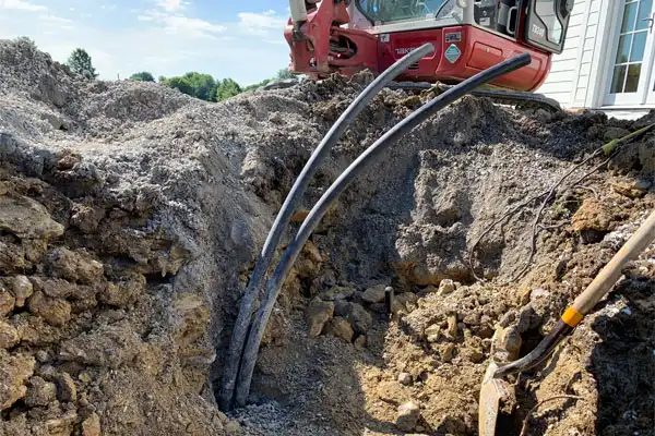 A construction site with three exposed black cables emerging from the ground near an excavator. A shovel is visible on the right.