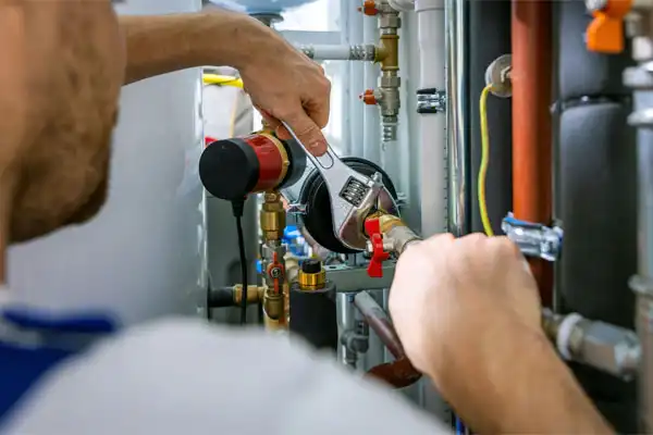 Person using a wrench to tighten a pipe in a boiler room.