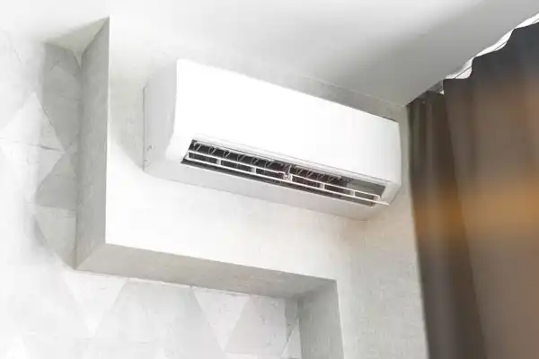 Wall-mounted air conditioning unit installed above a window with dark curtains.
