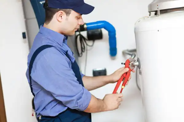 A person in a blue uniform and cap uses a wrench to adjust a valve on a white tank indoors.