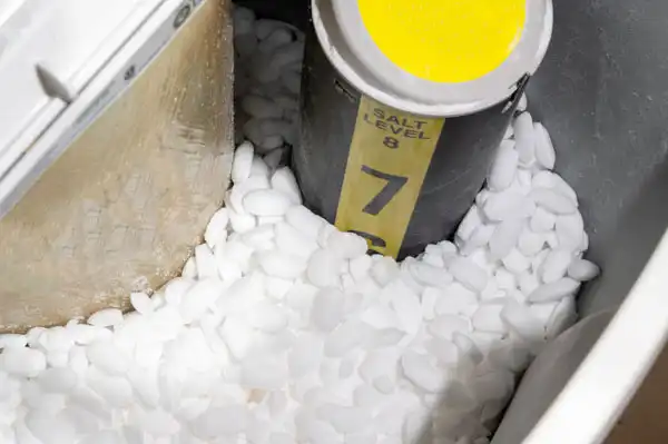 Water softener tank filled with salt pellets and a cylindrical marker showing the salt level.