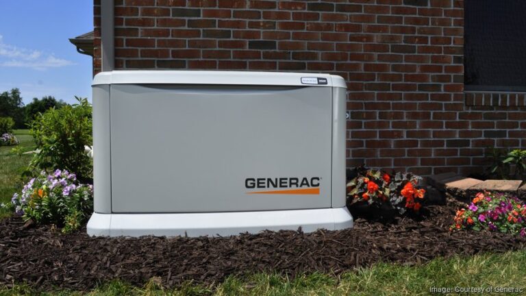 A Generac generator is installed on a landscaped area with flowers by a brick wall.